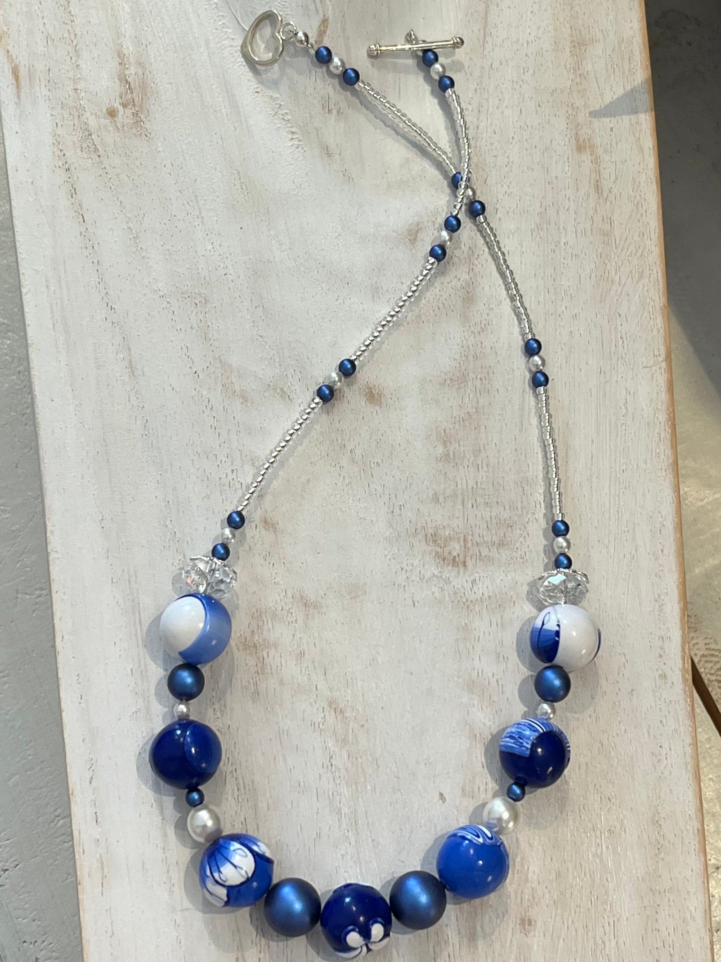 Seven-bead necklace from Stephanie Fraselle’s Marégraphie collection, featuring individually hand-sculpted polymer clay beads in sapphire, ultramarine, navy, white,accented with Swarovski crystals, pearls, Bohemian glass seed beads, and a 925 sterling silver heart toggle clasp, 51–52 cm length.