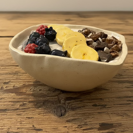 Hyperreal ceramic sculpture of a yogurt bowl with fruit and muesli, handmade in pottery with detailed raspberries, banana, blueberries, and chocolate