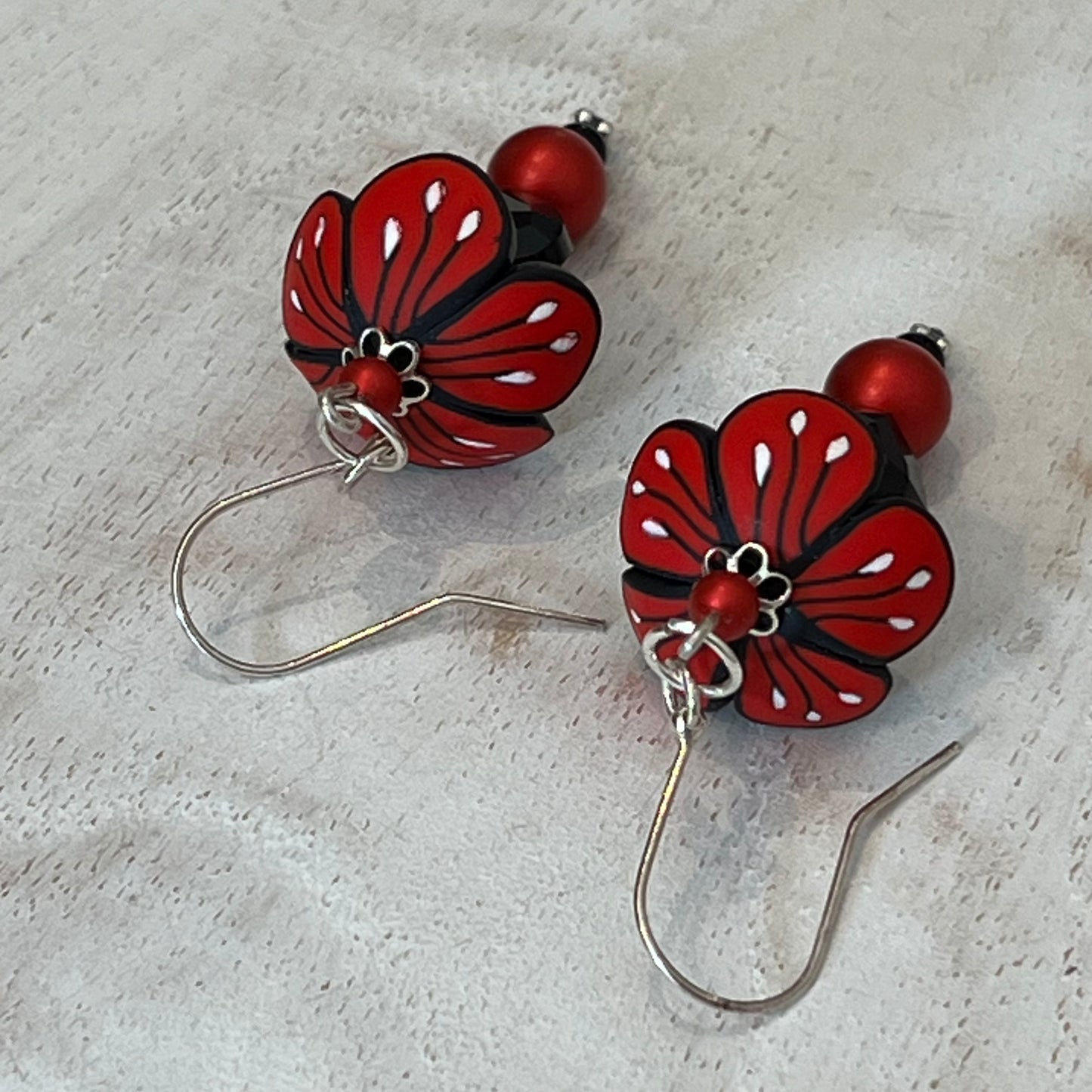 Close-up of Stephanie Fraselle’s Magic Moments Blossom Earrings – handcrafted red, white, and black polymer clay flowers with Swarovski crystal and pearl accents on sterling silver stems