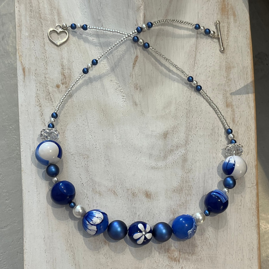 Seven-bead necklace from Stephanie Fraselle’s Marégraphie collection, featuring individually hand-sculpted polymer clay beads in sapphire, ultramarine, navy, white,accented with Swarovski crystals, pearls, Bohemian glass seed beads, and a 925 sterling silver heart toggle clasp, 51–52 cm length.