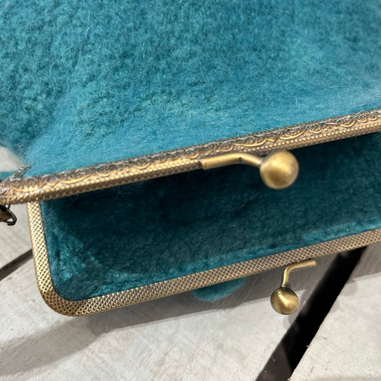 Handcrafted turquoise nuno-felted floral clutch made from 100% merino wool, featuring delicately felted flowers, brass kiss-lock clasp, and wool shoulder strap — artisan bag designed for special occasions and timeless everyday elegance.