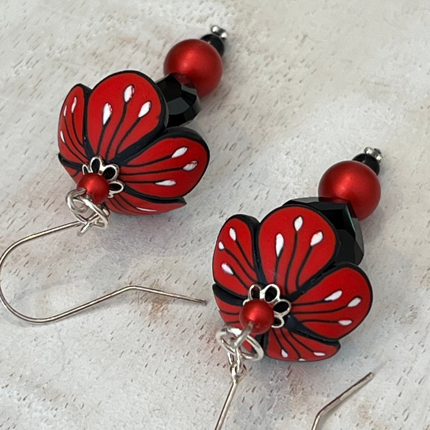 Close-up of Stephanie Fraselle’s Magic Moments Blossom Earrings – handcrafted red, white, and black polymer clay flowers with Swarovski crystal and pearl accents on sterling silver stems