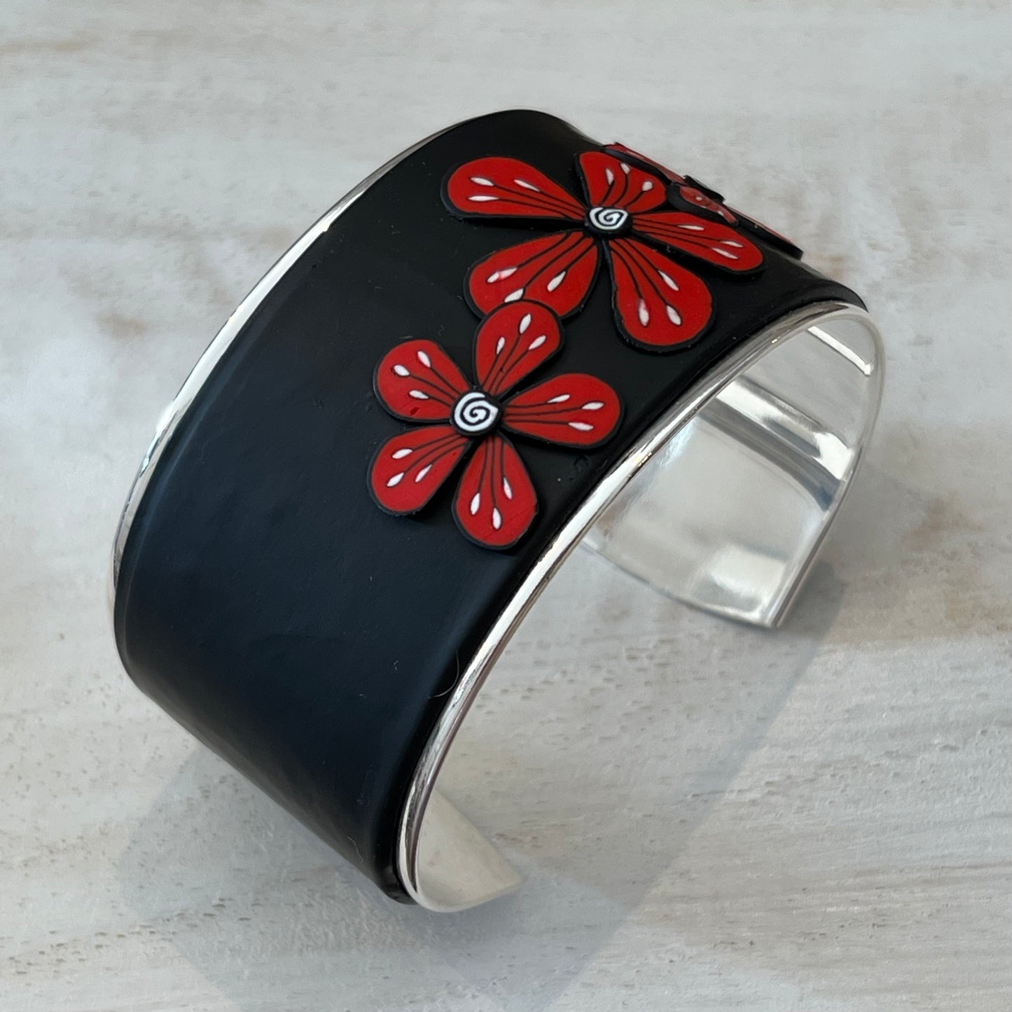 Unique handmade cuff by Lanzarote artisan Stephanie Fraselle featuring bold red and white floral accents on matte black polymer clay with silver-plated brass base