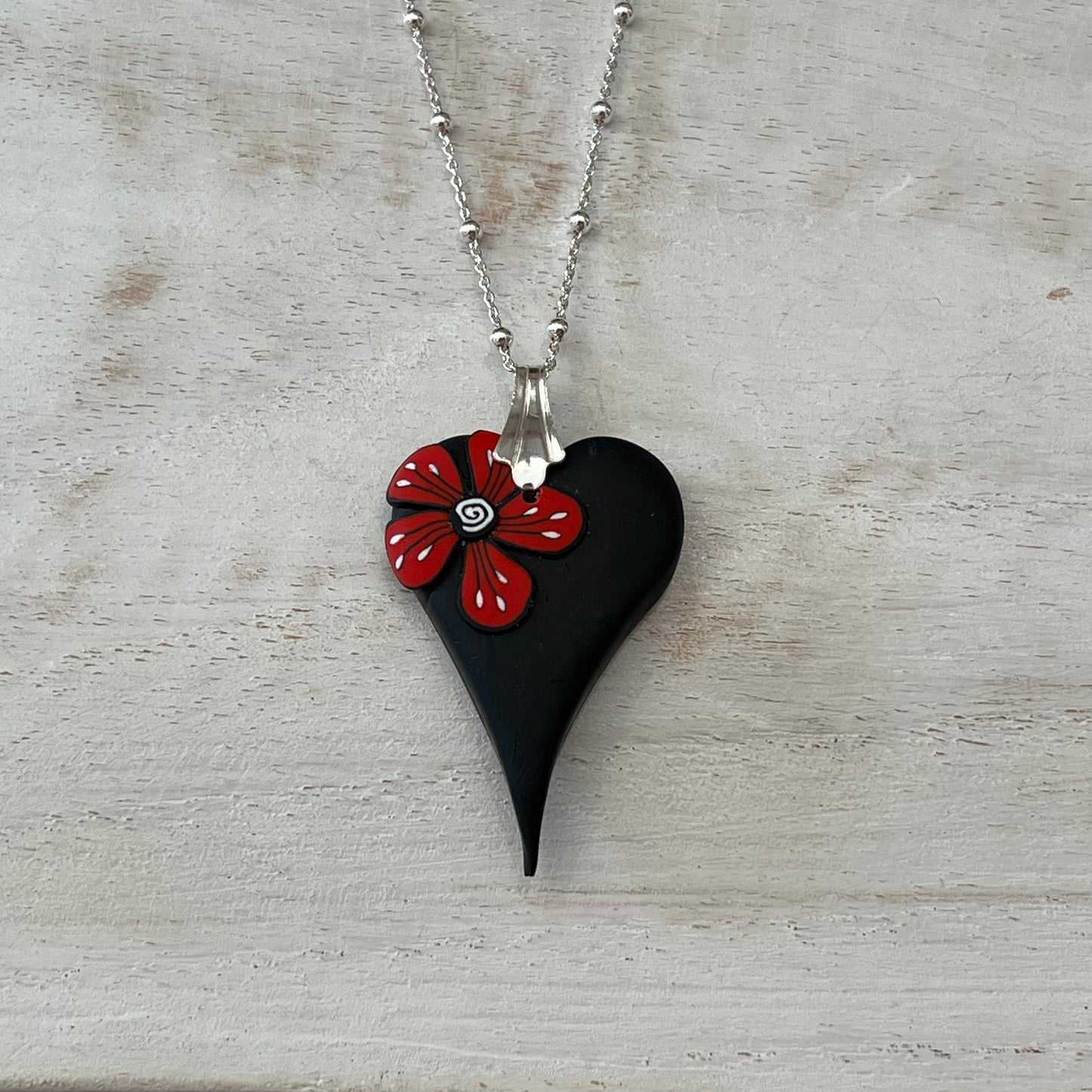 Handmade curved black heart pendant with red flower accent on sterling silver chain by Lanzarote artisan Stephanie Fraselle