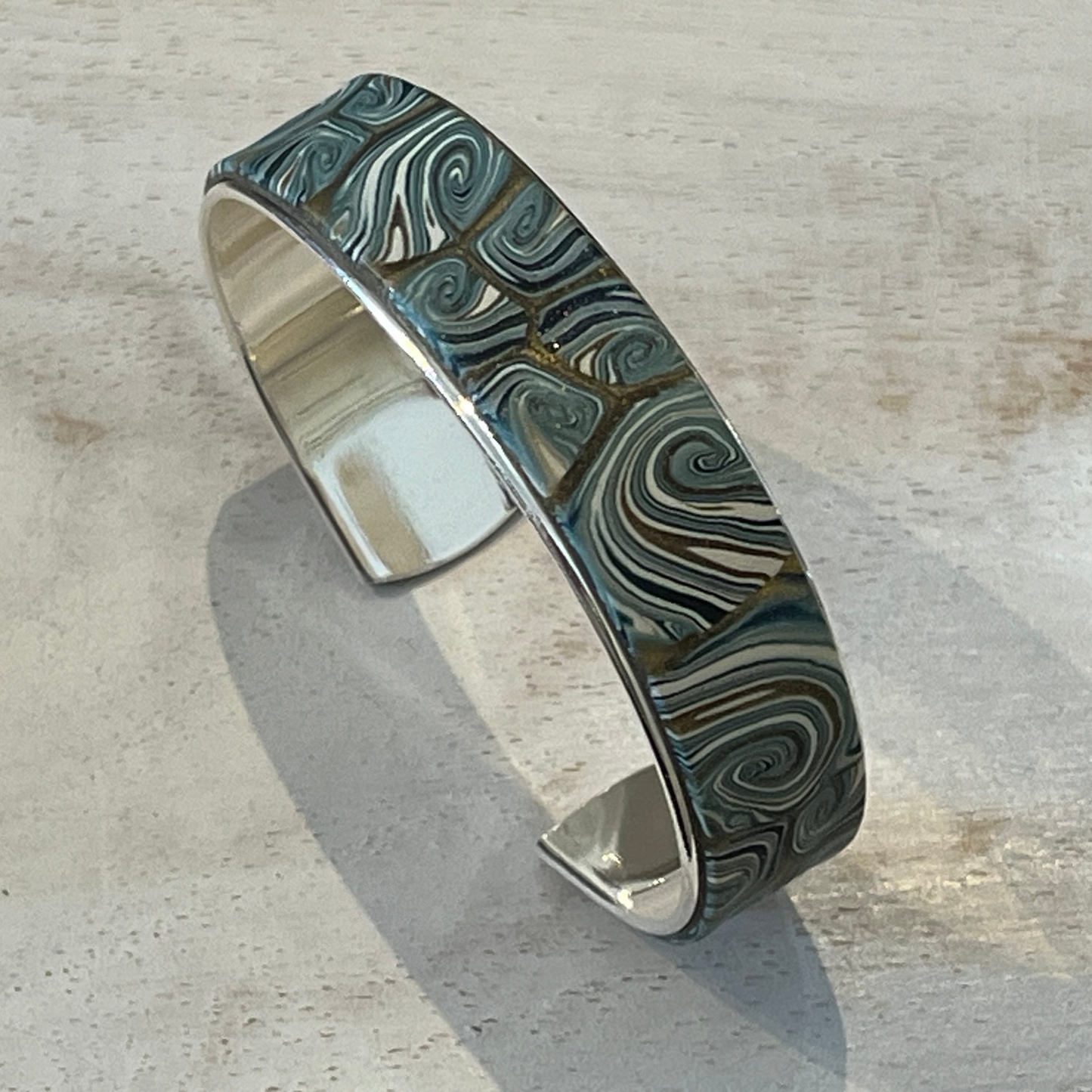 Handcrafted Nocturne cuff by Stephanie Fraselle in sterling silver-coated brass with gold, pearlescent, and petrol blue tones