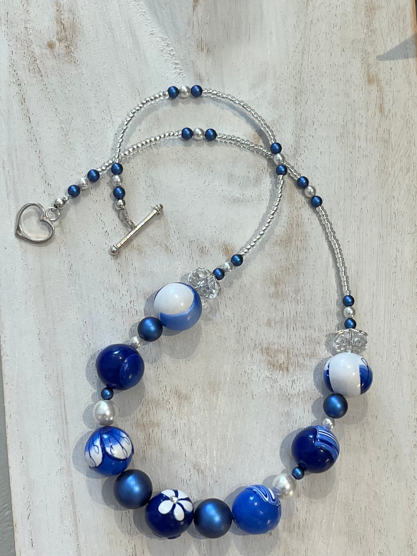 Seven-bead necklace from Stephanie Fraselle’s Marégraphie collection, featuring individually hand-sculpted polymer clay beads in sapphire, ultramarine, navy, white,accented with Swarovski crystals, pearls, Bohemian glass seed beads, and a 925 sterling silver heart toggle clasp, 51–52 cm length.