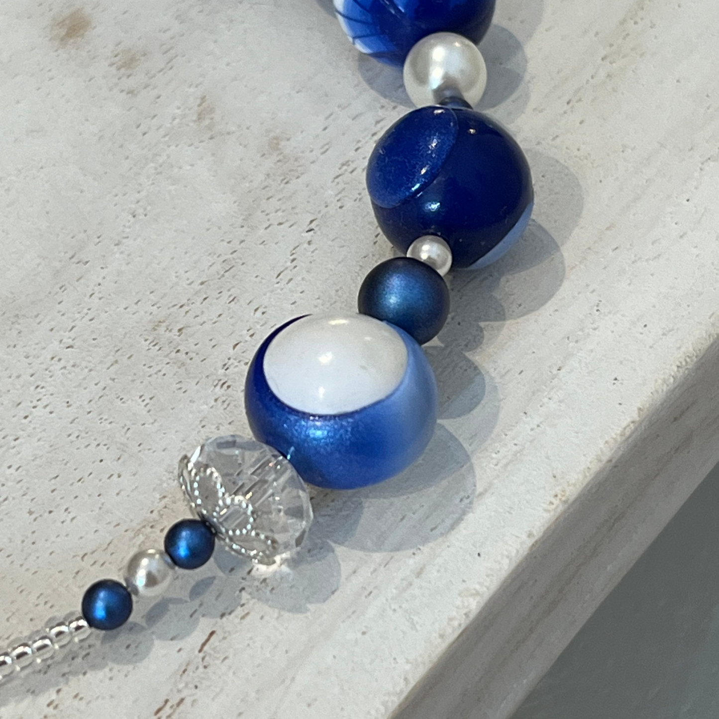 Seven-bead necklace from Stephanie Fraselle’s Marégraphie collection, featuring individually hand-sculpted polymer clay beads in sapphire, ultramarine, navy, white,accented with Swarovski crystals, pearls, Bohemian glass seed beads, and a 925 sterling silver heart toggle clasp, 51–52 cm length.