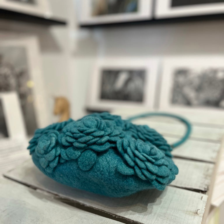 Handcrafted turquoise nuno-felted floral clutch made from 100% merino wool, featuring delicately felted flowers, brass kiss-lock clasp, and wool shoulder strap — artisan bag designed for special occasions and timeless everyday elegance.