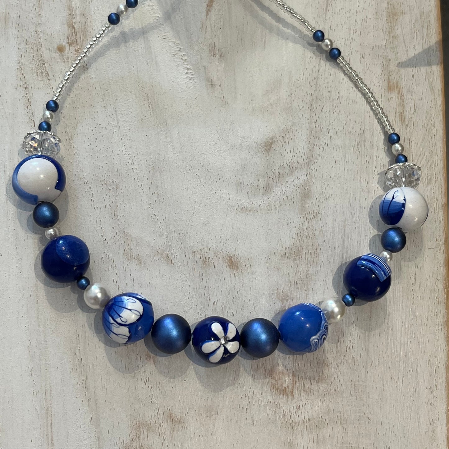 Seven-bead necklace from Stephanie Fraselle’s Marégraphie collection, featuring individually hand-sculpted polymer clay beads in sapphire, ultramarine, navy, white,accented with Swarovski crystals, pearls, Bohemian glass seed beads, and a 925 sterling silver heart toggle clasp, 51–52 cm length.
