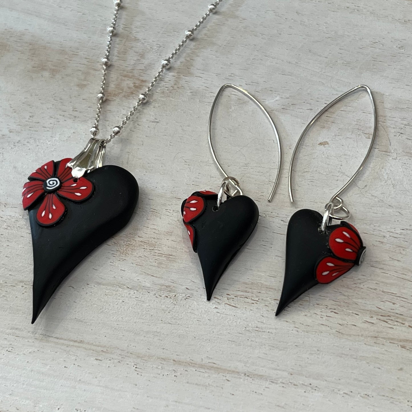 Handcrafted black heart-shaped earrings with red flower detail by Lanzarote artisan Stephanie Fraselle, paired with matching pendant (sold separately)