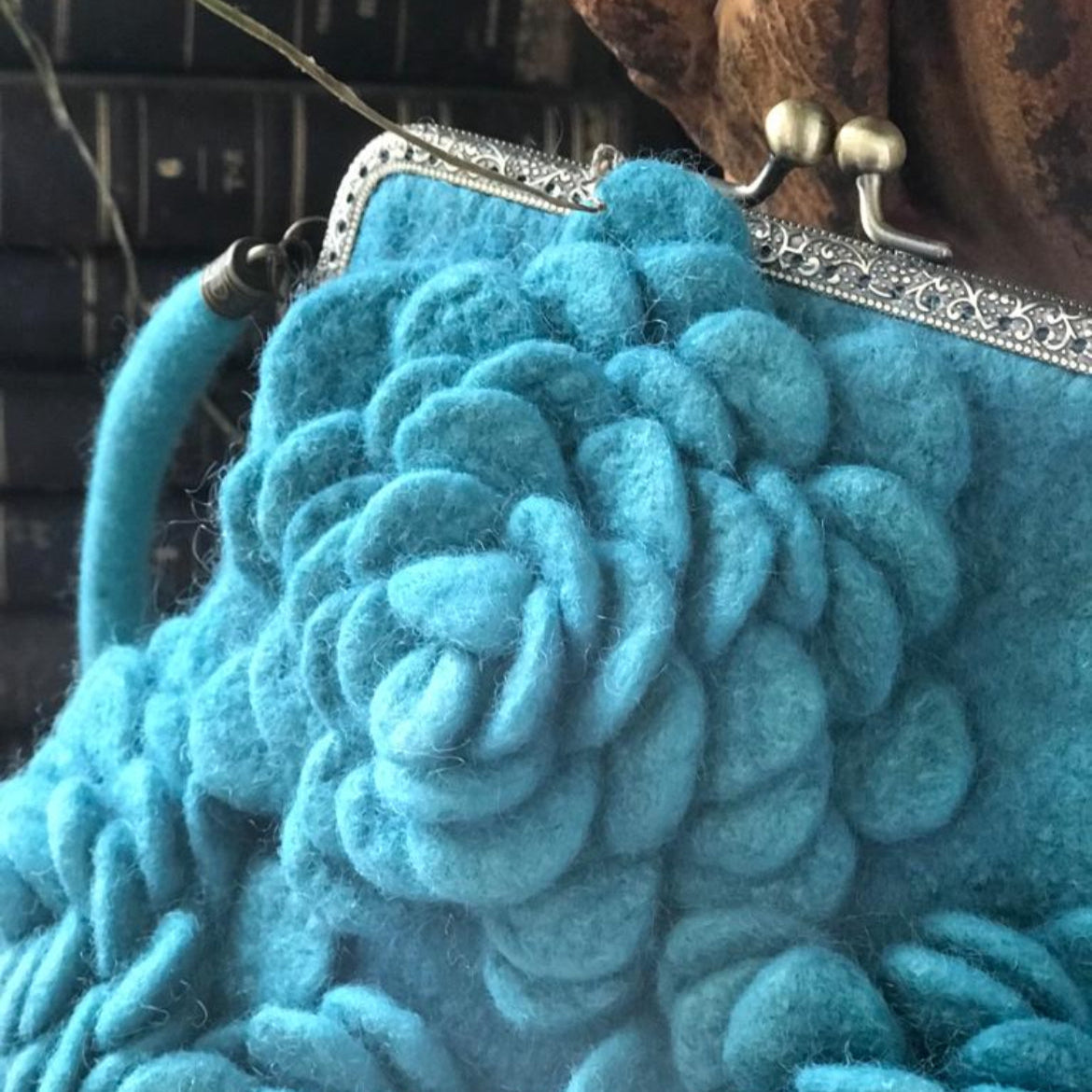 Handcrafted turquoise nuno-felted floral clutch made from 100% merino wool, featuring delicately felted flowers, brass kiss-lock clasp, and wool shoulder strap — artisan bag designed for special occasions and timeless everyday elegance.