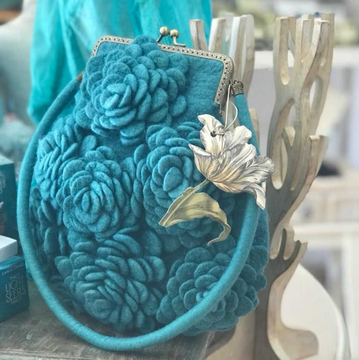 Handcrafted turquoise nuno-felted floral clutch made from 100% merino wool, featuring delicately felted flowers, brass kiss-lock clasp, and wool shoulder strap — artisan bag designed for special occasions and timeless everyday elegance.