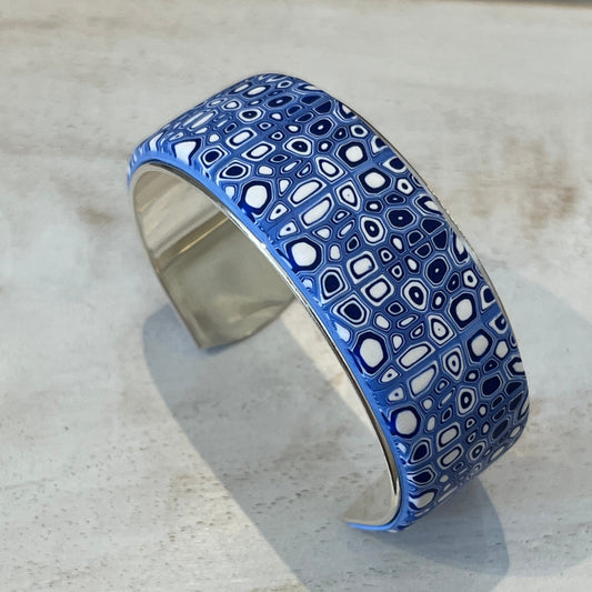 A handcrafted adjustable cuff from Stephanie Fraselle’s Ocean Shimmer collection, featuring an intricate mosaic of tiny, unique cells in sapphire blue, navy, ultramarine, and white. The polymer clay design is set in Sterling Silver 925 over brass, 23 mm wide, 14.5 cm long, lead-, cadmium-, and nickel-free.