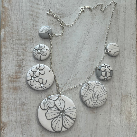 The Seven necklace from the White Blossom Collection by Stephanie Fraselle featuring seven handcrafted polymer clay medallions with botanical motifs, Swarovski crystals, and pearls on a sterling silver chain.
