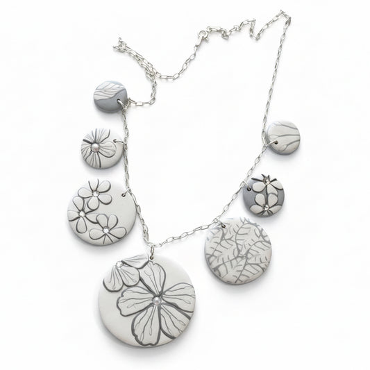 The Seven necklace from the White Blossom Collection by Stephanie Fraselle featuring seven handcrafted polymer clay medallions with botanical motifs, Swarovski crystals, and pearls on a sterling silver chain.