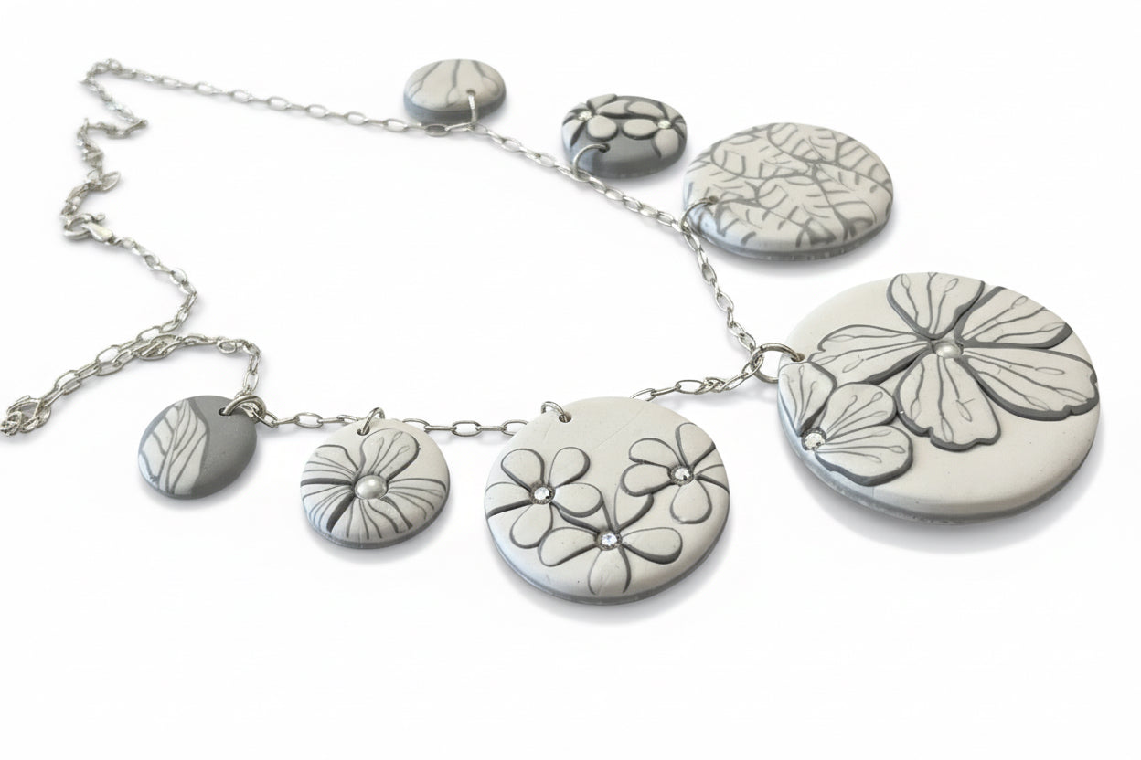 The Seven necklace from the White Blossom Collection by Stephanie Fraselle featuring seven handcrafted polymer clay medallions with botanical motifs, Swarovski crystals, and pearls on a sterling silver chain.