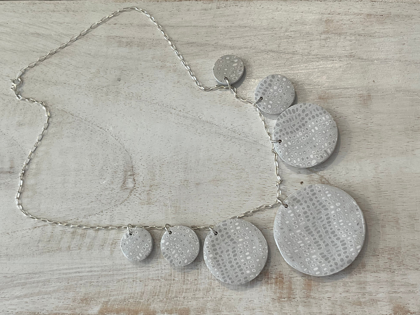 The Seven necklace from the White Blossom Collection by Stephanie Fraselle featuring seven handcrafted polymer clay medallions with botanical motifs, Swarovski crystals, and pearls on a sterling silver chain.