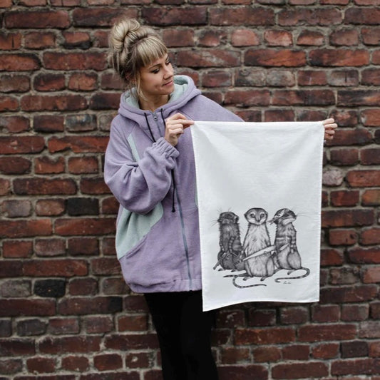Black and white illustration of three meerkats standing tall, one with a bandana, one holding a baseball, on a linen tea towel