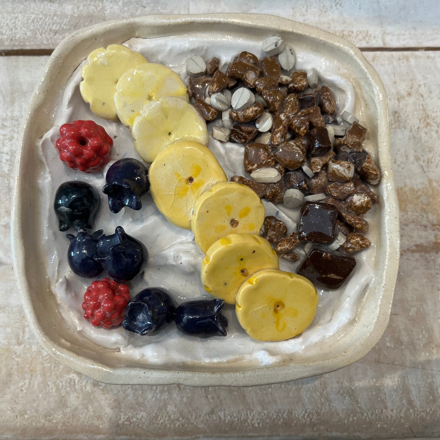 Hyperreal ceramic sculpture of a yogurt bowl with fruit and muesli, handmade in pottery with detailed raspberries, banana, blueberries, and chocolate