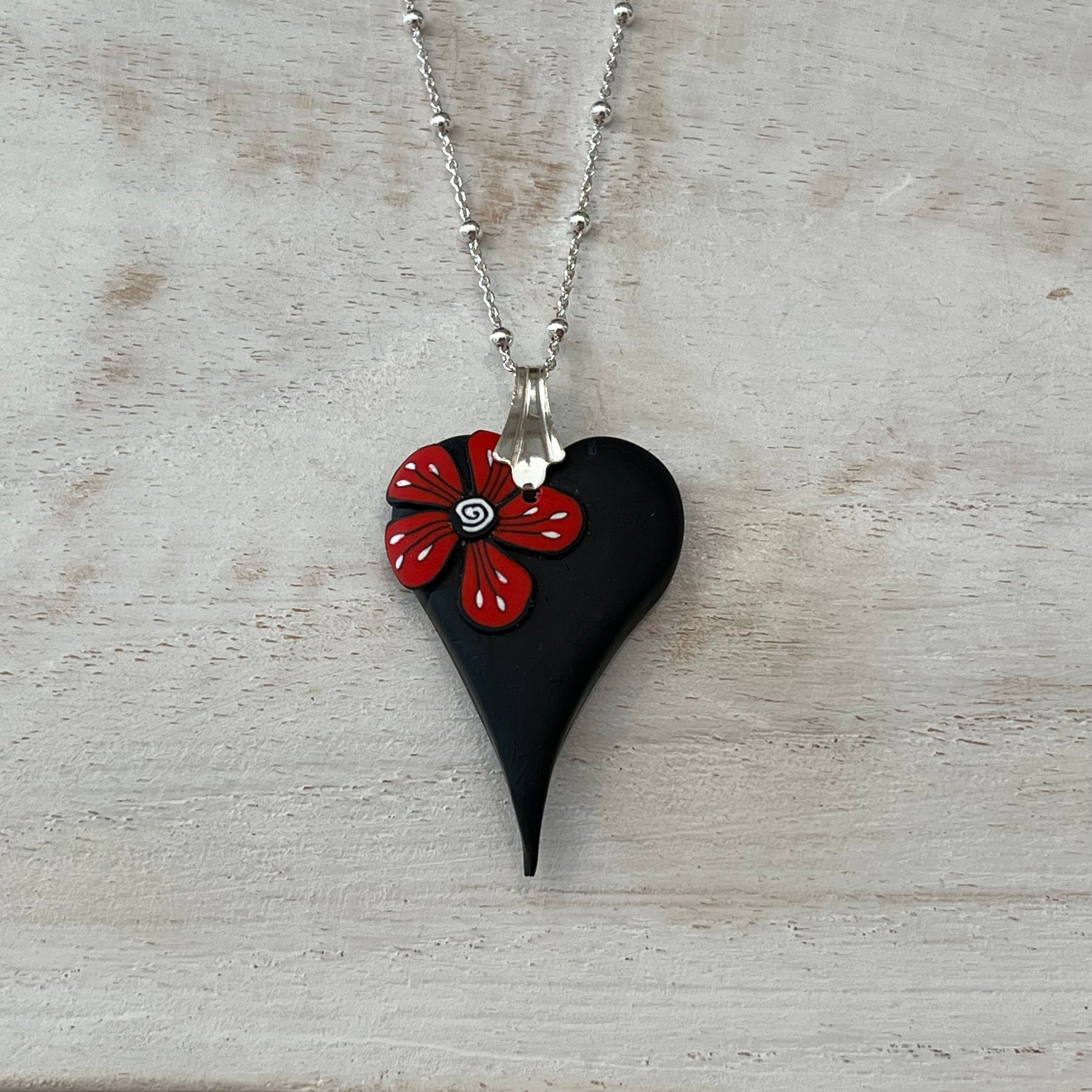 Handmade curved black heart pendant with red flower accent on sterling silver chain by Lanzarote artisan Stephanie Fraselle