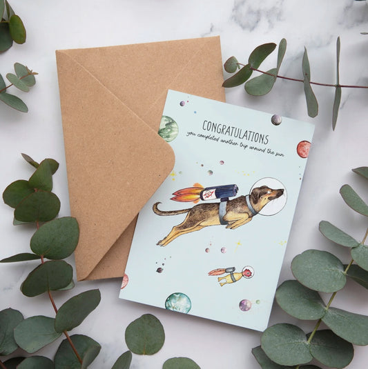 Bamboo greeting card featuring Lottie the dog floating in space with the message “Congratulations, you have completed another trip around the sun”