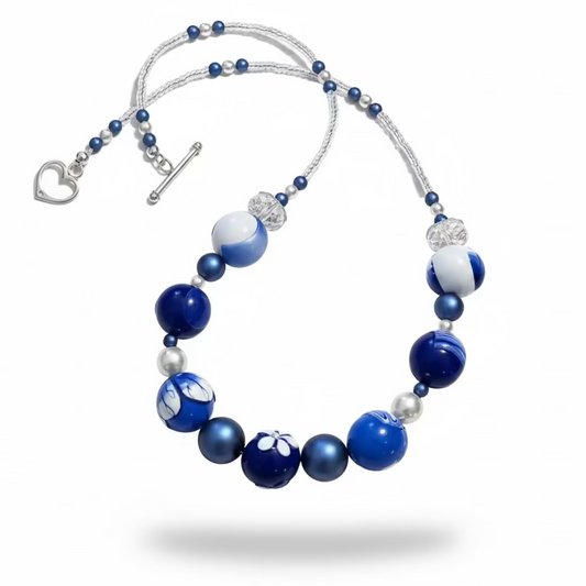 Seven-bead necklace from Stephanie Fraselle’s Marégraphie collection, featuring individually hand-sculpted polymer clay beads in sapphire, ultramarine, navy, white,accented with Swarovski crystals, pearls, Bohemian glass seed beads, and a 925 sterling silver heart toggle clasp, 51–52 cm length.