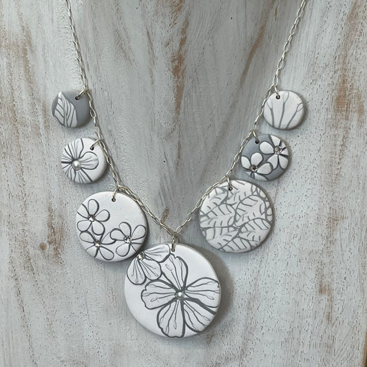The Seven necklace from the White Blossom Collection by Stephanie Fraselle featuring seven handcrafted polymer clay medallions with botanical motifs, Swarovski crystals, and pearls on a sterling silver chain.