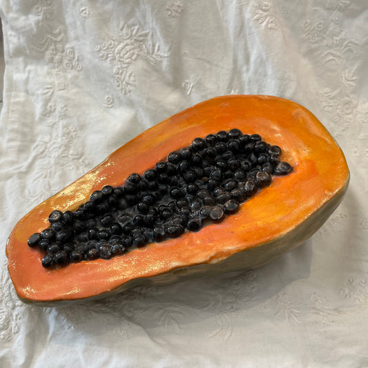 Hyperreal ceramic sculpture of halved papaya with glistening seeds in lifelike detail