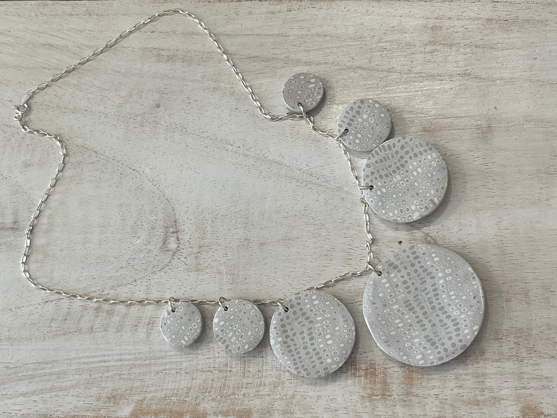 The Seven necklace from the White Blossom Collection by Stephanie Fraselle featuring seven handcrafted polymer clay medallions with botanical motifs, Swarovski crystals, and pearls on a sterling silver chain.